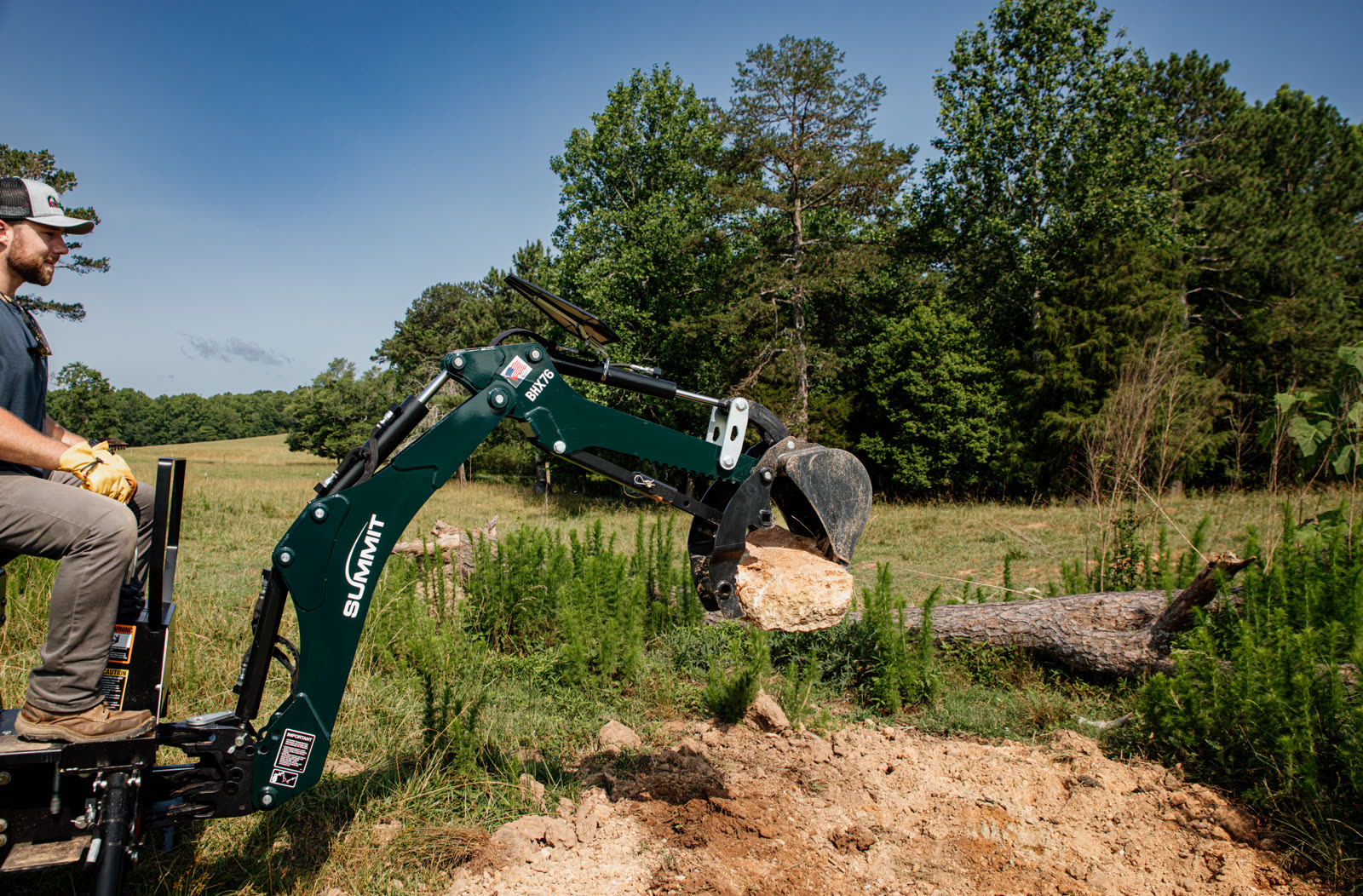 BHX76 backhoe lifting a boulder in open field